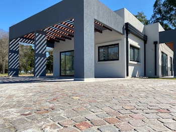 Casa de diseño moderno con paredes grises y blancas, ventanas con marcos negros, una pérgola de vigas y un suelo de adoquines