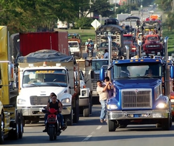 Vista frontal de una carretera congestionada con múltiples camiones de carga de diferentes colores y motocicletas. Se ven personas en los vehículos