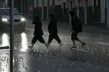 Varias personas caminan empapadas por una calle de Palma durante el paso de la DANA Adam. (Miquel A. Borràs/EFE)