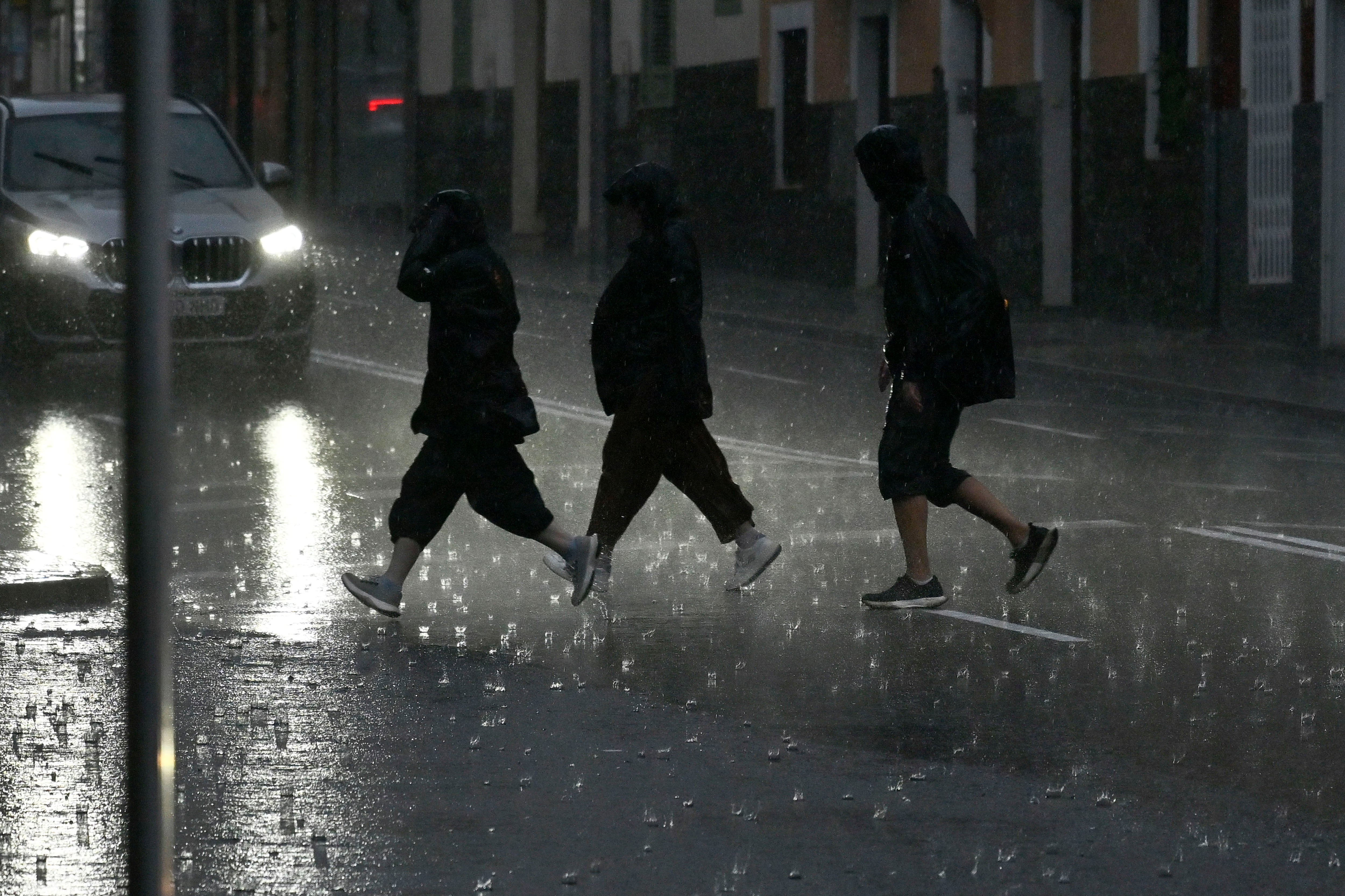 Varias personas caminan empapadas por una calle de Palma durante el paso de la DANA Adam. (Miquel A. Borràs/EFE)