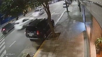 Toma de cámara de seguridad nocturna que muestra una acera y una calle con vehículos en movimiento y un automóvil estacionado