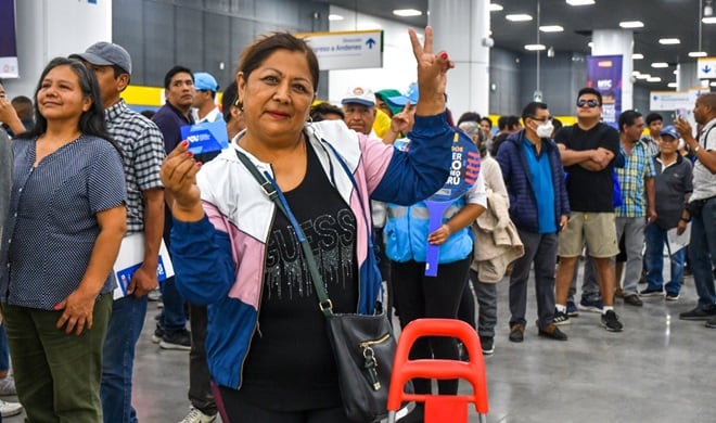 Una usuaria del Metro de Lima muestra su tarjeta de transporte mientras hace una señal de victoria en una estación concurrida de la ciudad. (ATU)