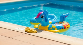 Una piscina con agua azul, un flotador infantil de caballo azul y amarillo, y un par de sandalias amarillas en el borde.