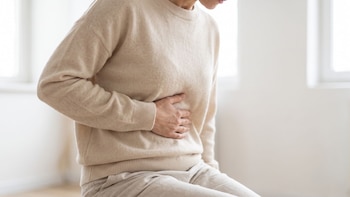 Torso de una persona con jersey beige que coloca la mano sobre su abdomen dentro de una habitación clara