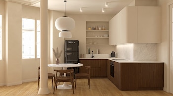 Interior de una cocina moderna y un área de comedor. Se ven gabinetes de madera oscura y blancos, encimeras de mármol, un refrigerador Smeg y mesa con sillas de madera.