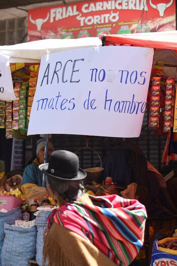 Una mujer camina en un mercado de La Paz, en Bolivia, el 21 de octubre de 2024. En un letrero de fondo se lee "Arce, no nos mates de hambre". REUTERS/Claudia Morales