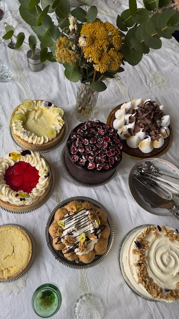 Vista superior de una mesa con varios pasteles y tartas, un florero con plantas y cubiertos al lado de un plato