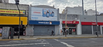 Vista frontal de una calle urbana con edificios comerciales. La farmacia Dr. Ahorro aparece cerrada con persianas metálicas. Personas caminan por la acera