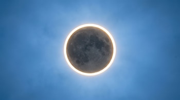Eclipse solar anular mostrando la Luna oscura frente al Sol, que forma un anillo brillante de luz dorada. El cielo es azul y claro.
