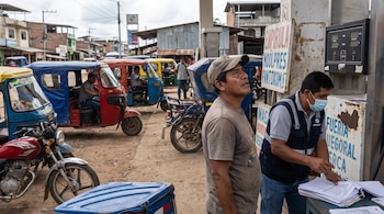 Hombres junto a mototaxis y un dispensador de combustible en una calle de tierra. Un trabajador manipula papeles, otro hombre mira al cielo