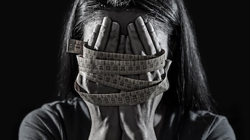 close up hands wrapped in tailor measure tape covering face of young depressed and worried girl suffering anorexia or bulimia nutrition disorder on black background obsessed with diet and overweight