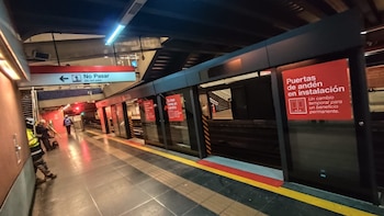 Andén de estación de metro con paneles de puertas en instalación, letreros rojos de advertencia y trabajadores con cascos de seguridad