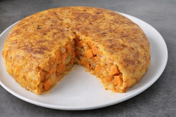 Primer plano de una tortilla redonda de boniato y cebolla con una porción cortada. El interior muestra dados de boniato naranja y trozos de cebolla blanca.