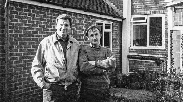 El periodista Ben Macintyre posa junto al exoficial del KGB Vladimir Kuzichkin frente a una vivienda de ladrillos. (The Economist)