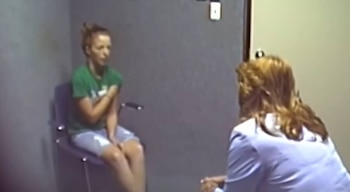 En una sala, Amber Wright, de cabello recogido y camiseta verde, se sienta frente a una mujer rubia de espaldas, probablemente una oficial