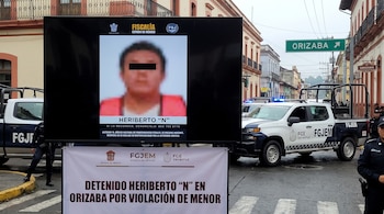 Pantalla con foto censurada de un hombre y texto. Cartel blanco de detención. Dos patrullas policiales y agentes en una calle de Orizaba con edificios.