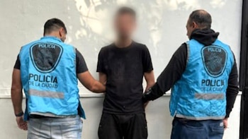 Hombre con rostro borroso, vestido de negro, siendo sujetado por dos policías de la Ciudad con chalecos azules que lo flanquean