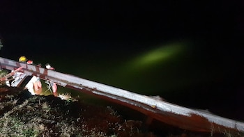 Personal de emergencia con uniformes y cascos junto a una barrera metálica de carretera con cinta de 'Peligro', parcialmente en agua bajo la noche