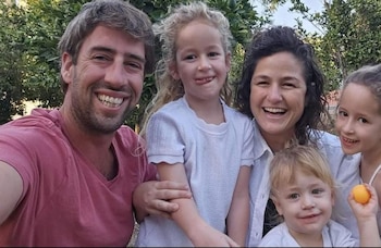 Un hombre, una mujer y tres niños sonríen juntos en un entorno exterior con vegetación de fondo
