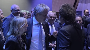 Varias personas con traje formal conversan en un salón con iluminación azulada durante un evento oficial