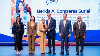 Luis Abinader y cuatro personas posan en un escenario mientras entregan un trofeo a una mujer frente a una pantalla digital azul