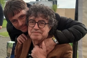 Juan De Benedictis abraza por la espalda a Piero De Benedictis, quien lleva gafas y una chaqueta marrón