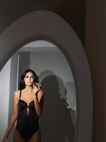 Zaira Nara, de cabello oscuro y lencería negra, se mira en un espejo grande y arqueado mientras toma una foto con una cámara compacta