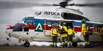 Helicóptero blanco, azul y rojo con logos INFOCA y Avincis. Varios hombres con uniformes amarillos y cascos verdes suben al helicóptero