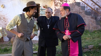 Tres hombres vestidos como un campesino con sombrero, un sacerdote y un arzobispo sostienen una discusión frente a una vivienda rural