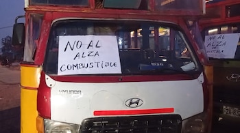 Frente de un vehículo de transporte público rojo y blanco con un cartel que dice "NO AL ALZA COMBUSTIBLE", logo Hyundai. Otro vehículo similar aparece a la derecha