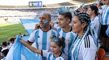 Una familia de cuatro hinchas argentinos, incluyendo un hombre, dos niños y una mujer, con peinados y caras pintadas de celeste y blanco en las gradas de un estadio.