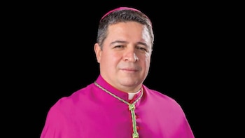 Retrato de um bispo vestindo capa e caveira fúcsia, olhando para cima com um pequeno sorriso. Faça um cordão ritual