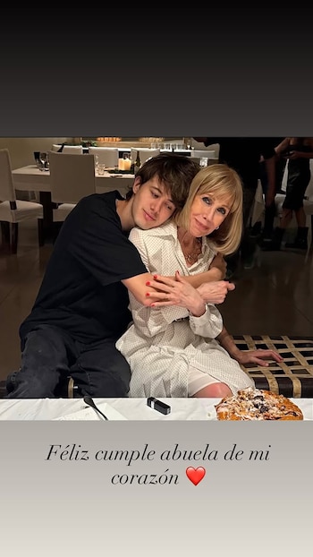 Evangelina Salazar, una mujer rubia con un vestido blanco con puntos, sonríe abrazada por un joven de cabello castaño en una mesa de comedor