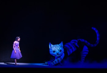 Mujer en vestido morado con diadema blanca y gato azul con rayas negras y ojos grandes, iluminados por luz azul en un escenario oscuro con niebla
