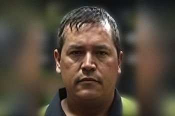 Primer plano de un hombre de cabello corto y oscuro que viste una camisa con cuello negro y prendas verdes.