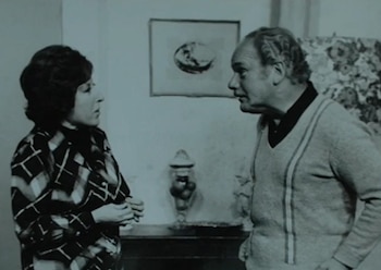 Una imagen monocromática muestra a Nelly Láinez y Marcos Zucker de perfil, de pie e interactuando en interiores, con arte y un jarrón al fondo