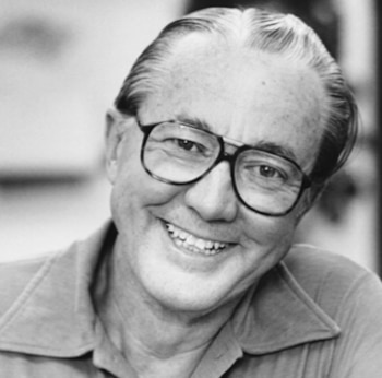 Retrato en blanco y negro de un hombre sonriente con gafas. El hombre tiene el pelo corto, peinado hacia atrás