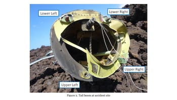 Primer plano del botalón de cola dañado de un helicóptero, con su estructura interna y cables expuestos, sobre un terreno rocoso oscuro y cielo azul
