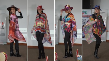 Cuatro mujeres modelan con sombreros de ala ancha y ponchos coloridos con estampados, pantalones negros y botas. Hay una bandera peruana y una pantalla con logo