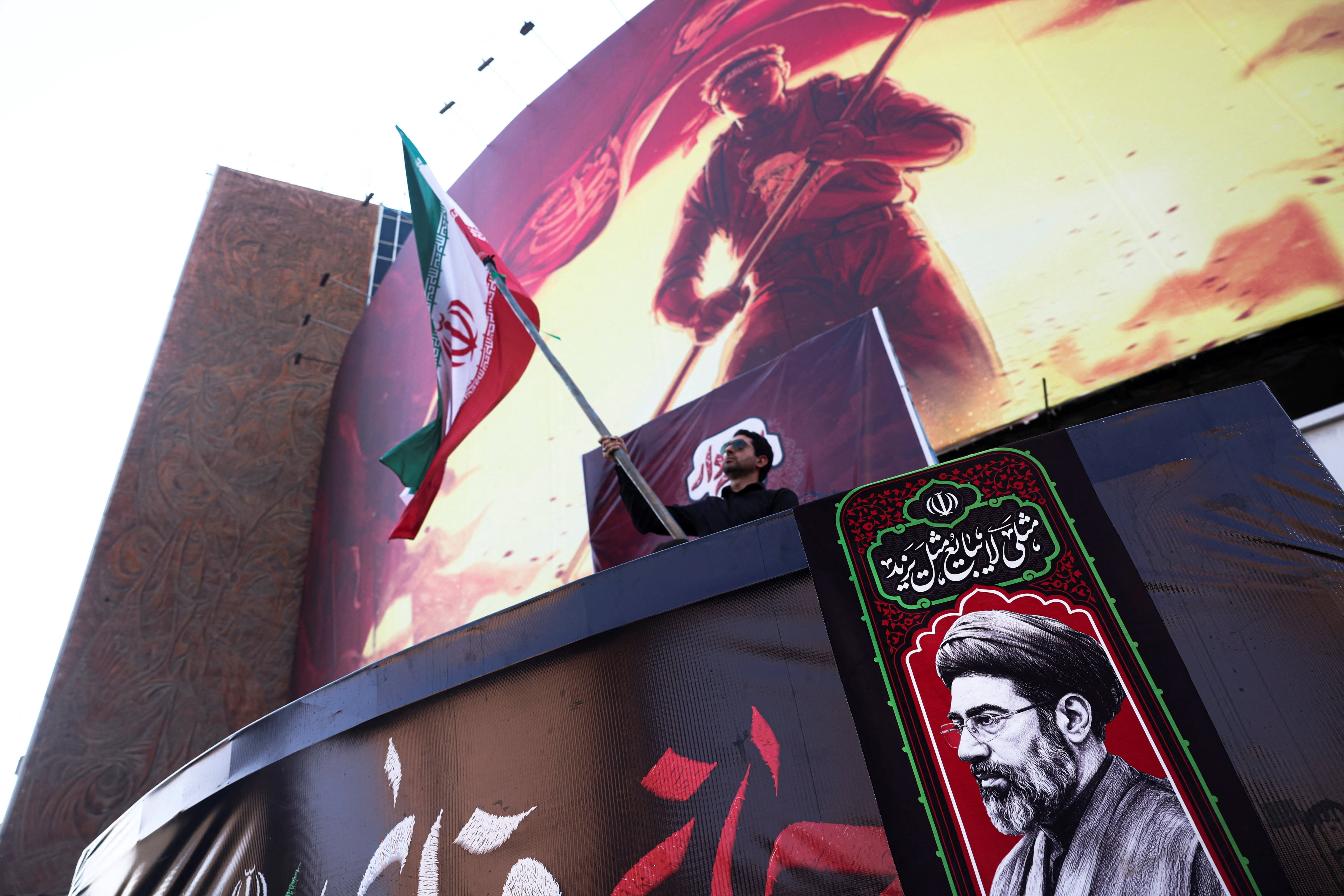 Un hombre sostiene una bandera iraní junto a una fotografía del líder supremo de Irán, Mojtaba Jamenei, en Teherán (Majid Asgaripour/WANA vía REUTERS/archivo)