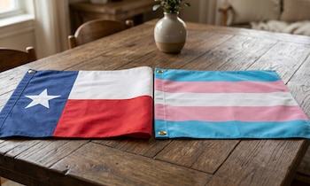 Dos banderas de tela sobre una mesa de madera. A la izquierda, la bandera de Texas. A la derecha, la bandera del orgullo trans, con franjas azul claro, rosa y blanca
