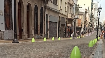 Una calle de adoquines con bolardos conicos verdes a los lados, farolas altas y fachadas de edificios de varios niveles.