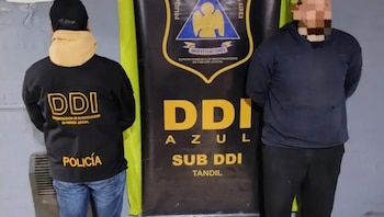 Un agente de policía de espaldas y un hombre con el rostro pixelado permanecen de pie junto a un banner institucional de la fuerza de seguridad