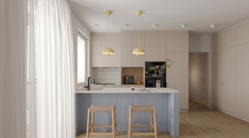 Cocina con isla, dos taburetes, gabinetes claros, horno, fregadero, grifo, ventana, cortinas y lámparas colgantes amarillo pálido.