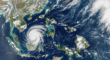 Mapa satelital con grandes masas de nubes, varias islas de color verde y una tormenta ciclónica en espiral blanca sobre el océano.