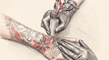 Primer plano de dos manos con guantes negros haciendo un tatuaje con máquina sobre un antebrazo humano que tiene diseños de flores y patrones.