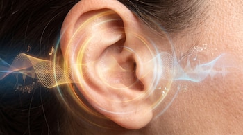 Primer plano de un oído humano junto a cabello oscuro. Ondas de sonido y notas musicales de colores amarillo, azul y blanco salen del oído.