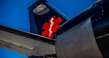 Cola de un avión azul oscuro con el símbolo rojo de la Estrella de la Vida impreso en el costado sobre un cielo despejado