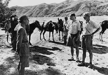 Fotografía en blanco y negro de varias personas, incluyendo Norman Bethune, de pie junto a animales de carga en un paisaje desértico con montañas al fondo