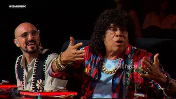 Primer plano de dos hombres sentados en un programa de televisión; uno con pelo rizado y camisa colorida gesticula, el otro calvo y con gafas sonríe